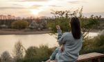 The view from the back of the girl looks at the sunset, sitting on a bench.